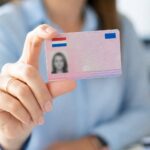 A person holding a Dutch driving license card with a blurred office background.