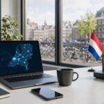 A modern office desk with a laptop, smartphone, and coffee cup, overlooking a Dutch cityscape with bicycles and traditional buildings.