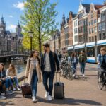 People walking and biking along a canal with traditional Dutch houses and a modern tram in the background.