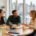 Three psychologists and counselors having a discussion around a table in a bright office with windows showing Amsterdam cityscape.
