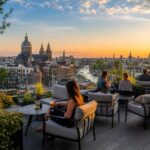 Rooftop bar with seating overlooking Amsterdam's canals and historic buildings during sunset.