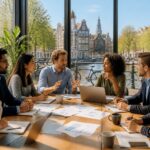 A diverse group of professionals having a meeting around a table with laptops and documents, with a view of Amsterdam canals and traditional buildings through large windows.