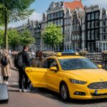A yellow taxi parked on a busy Amsterdam street with passengers boarding, surrounded by canal houses and bicycles.