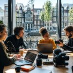 A group of young professionals working with media equipment in a bright workspace overlooking Amsterdam canals and historic buildings.