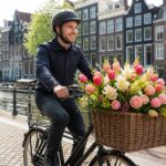 A delivery person on a bicycle carrying a basket full of fresh flowers in front of Amsterdam canal houses.