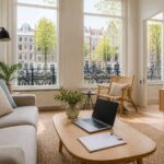 A bright living room in an Amsterdam Airbnb with large windows showing canal houses and bicycles outside.
