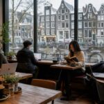 People working and relaxing inside a café in Amsterdam while rain falls outside the windows.