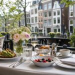 An outdoor brunch table set with elegant dishes and drinks in a quiet Amsterdam street with classic buildings and greenery.