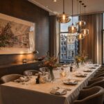 A private dining room with a long table set for a meal, large windows showing Amsterdam canal houses outside.