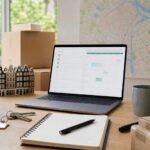 A workspace with a laptop, a map of Amsterdam, house keys, a pen, and a notebook arranged neatly on a desk.