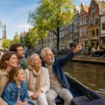 A family enjoying a boat ride on a canal in Amsterdam with traditional houses, bicycles, and outdoor cafes along the water.