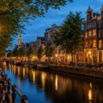 A calm evening scene along an Amsterdam canal with traditional houses, a cobblestone walkway, bicycles, and street lamps reflecting on the water.