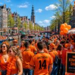 People celebrating King's Day on a street and canal in Amsterdam with orange decorations and traditional Dutch houses.