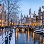 Snow-covered canal houses and bridges in Amsterdam with people walking along the streets during winter.