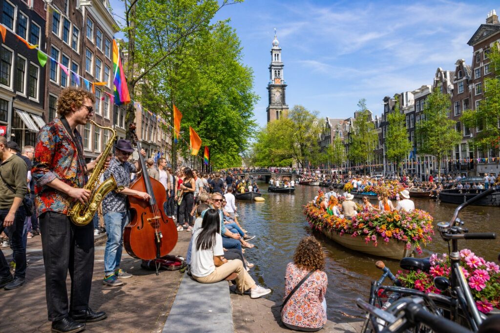 People enjoying a lively outdoor cultural festival along a canal with traditional Dutch houses and boats in Amsterdam.