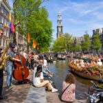 People enjoying a lively outdoor cultural festival along a canal with traditional Dutch houses and boats in Amsterdam.