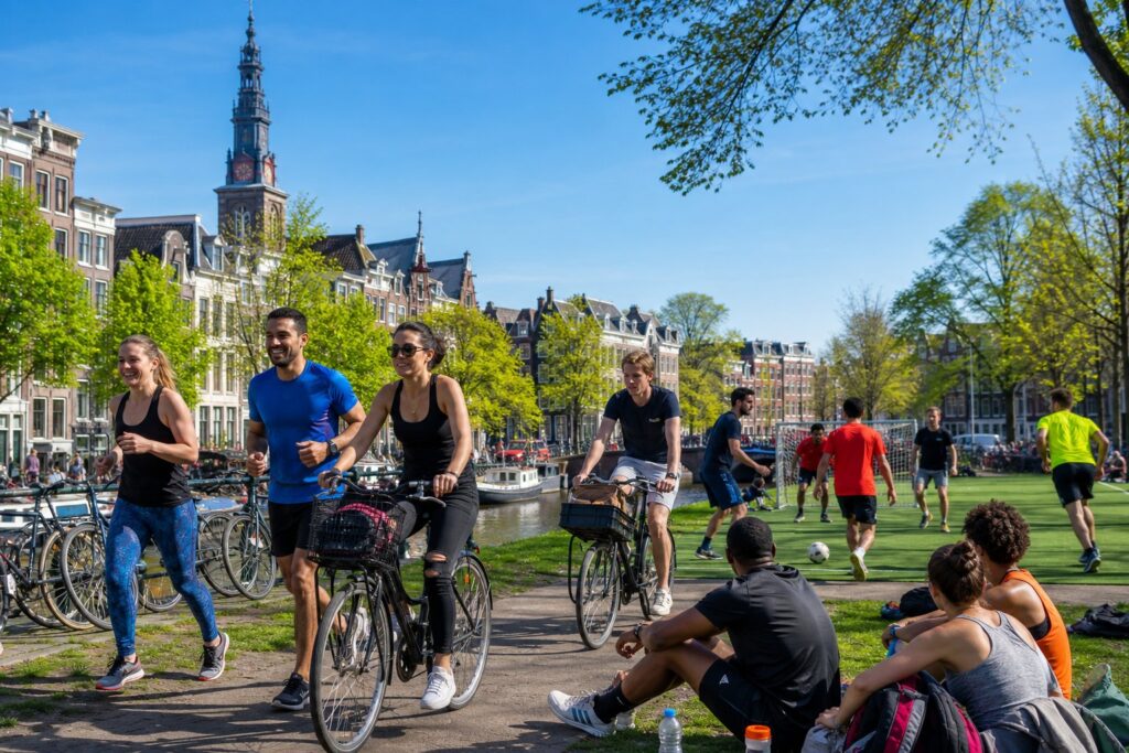 People participating in outdoor sports activities in a park with Amsterdam canal houses in the background.