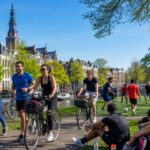 People participating in outdoor sports activities in a park with Amsterdam canal houses in the background.
