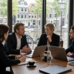 A small group of business professionals having a private meeting around a table with a canal and Amsterdam buildings visible through large windows.