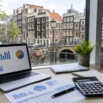 A workspace with a laptop, financial documents, and a calculator on a desk near a window showing Amsterdam canal houses and bicycles outside.