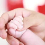 Newborn baby holding an adult finger