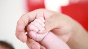 Newborn baby holding an adult finger