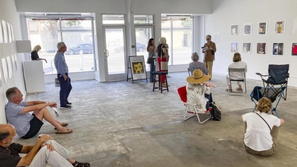 Visitors sitting and standing in a white-walled neighbourhood gallery