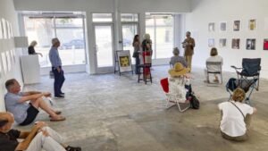 Visitors sitting and standing in a white-walled neighbourhood gallery