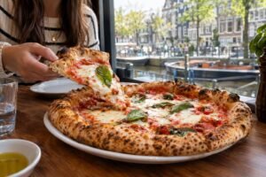 A diner reaches for a slice of pizza at a table beside an Amsterdam canal.