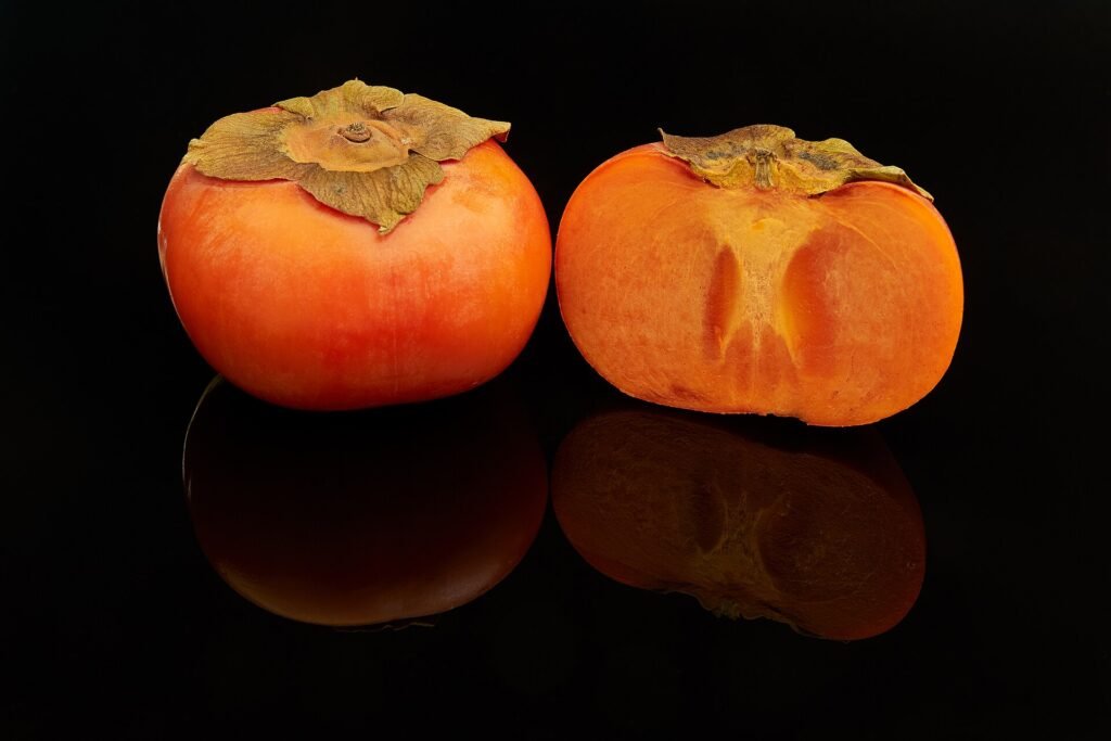 Two fuyu persimmon fruits, one cut in half