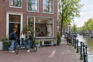 Students with bicycles outside a residence beside an Amsterdam canal.